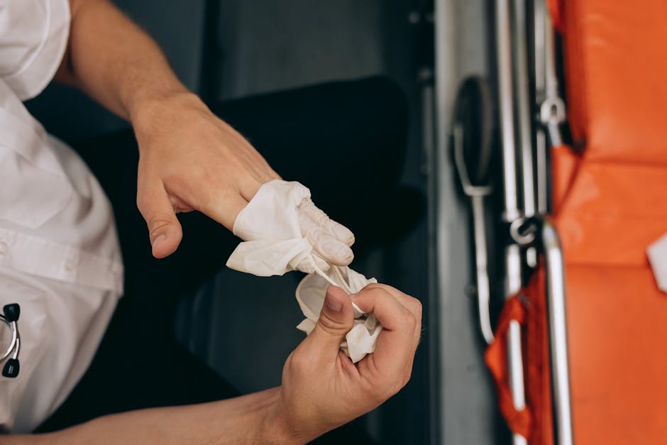 A close-up of a person's hands in the process of securely wrapping a piece of furniture with white protective fabric or plastic wrap, inside a vehicle or moving van. The individual is wearing a white shirt, and the image captures the detailed action of preparing furniture for safe transport during home relocation or moving tasks. In the background, there are visible tools and equipment such as metal bars, a red strap, and a blanket, indicating the loading and packing process involved in furniture transport. The scene is well-lit, highlighting the meticulous handling of the items for efficient packing and quick, professional removals by Man and Van Stepney, supporting their emergency same-day relocation services as described on the webpage for STEPNEY.